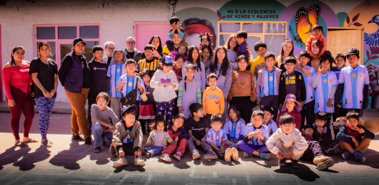 Group photo of the volunteers and children in front of the centre's mural