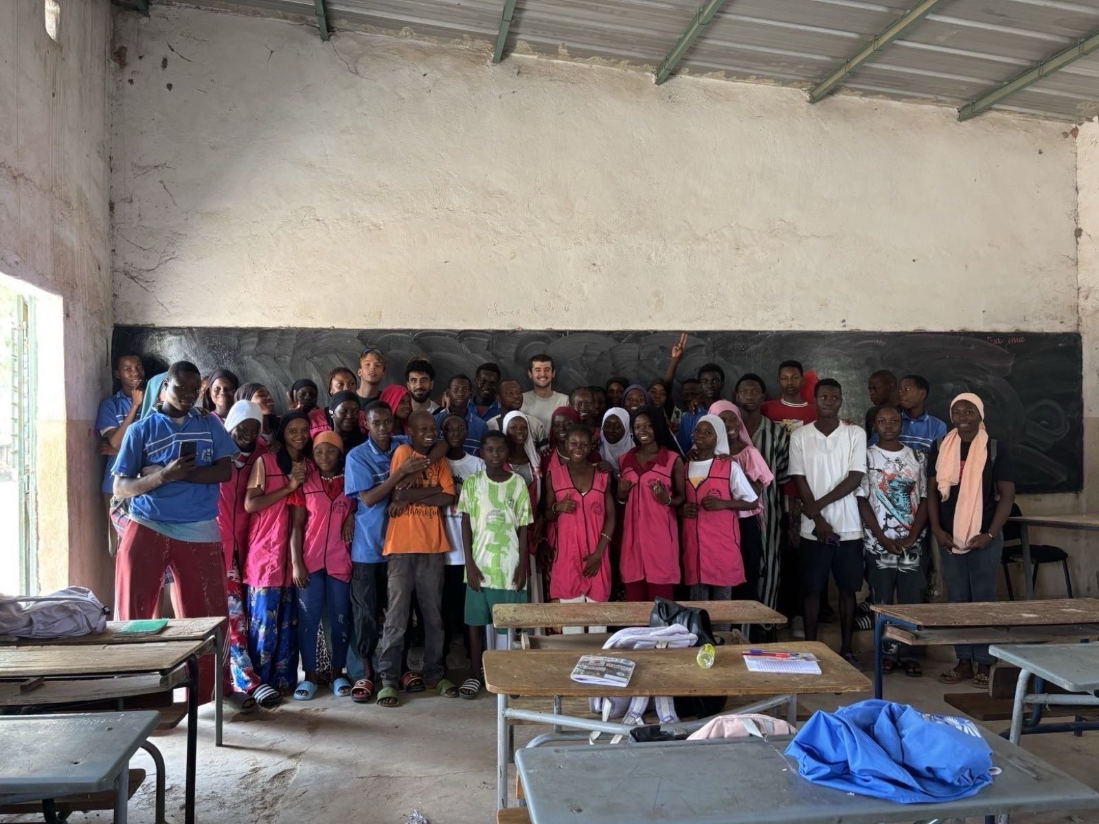 The volunteers with a class of pupils in pink and blue smocks, in front of the blackboard