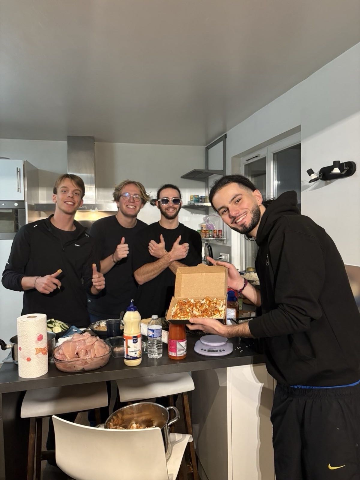 Four members of the association in the kitchen, thumbs up, showing a box of tasty crousty